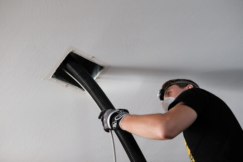 man in a black t-shirt cleaning out air vent with a black hose